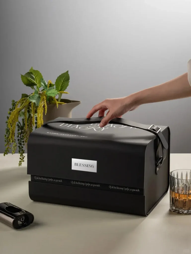 Person unboxing the BLESSING executive gift box featuring a luxury glass decanter, reusable cork stopper, branded whiskey glasses, and cooling stones.