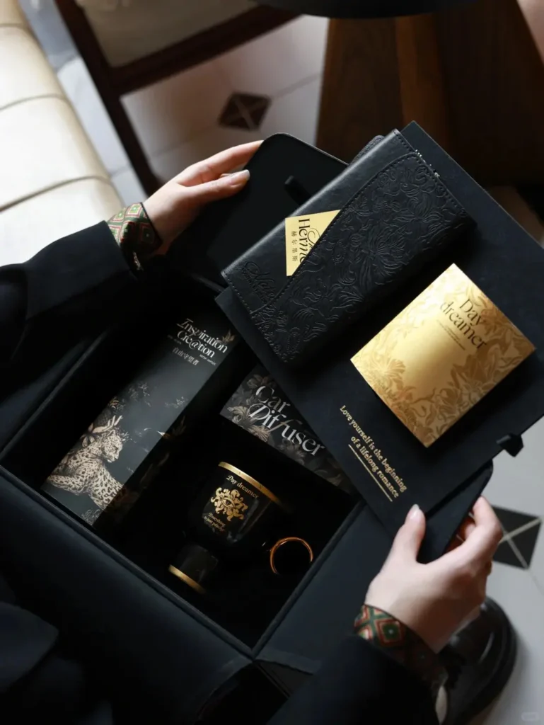 Person opening a luxury black leather gift box revealing high-end gifts including coffee mug, umbrella, wallet, car fragrance, and blessing envelope