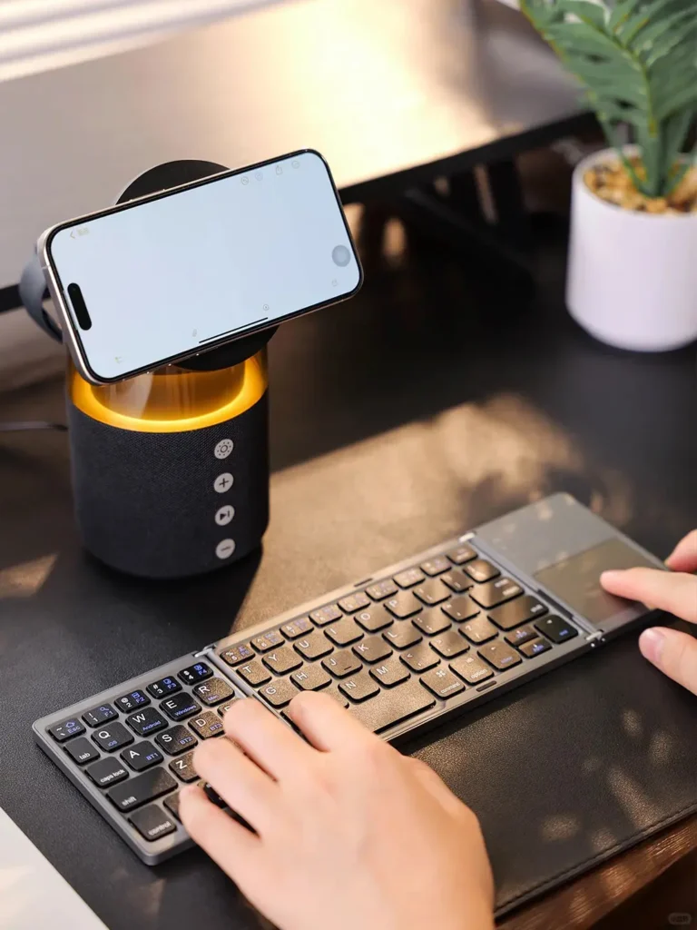 Tech-savvy corporate gift box on a desk with wireless charging smartphone, foldable keyboard being used, and person listening to music through Bluetooth speaker