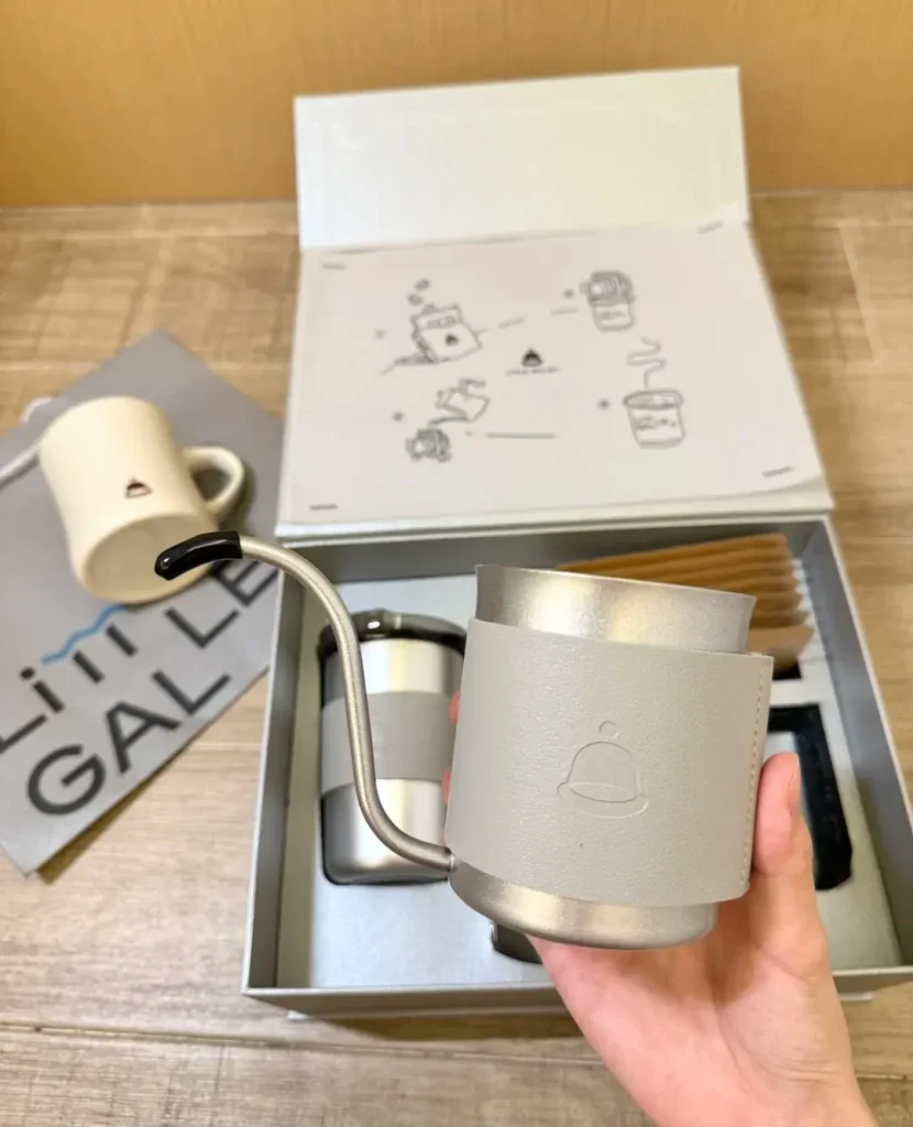 Person holding a hand-drip coffee pot above a silver-gray custom gift box from Xiamen Airlines. The box includes a simple line-drawing instruction sheet, insulated mug, ceramic mug, and tote bag. Perfect for customized gifts, custom gift boxes, and custom logo gifts, ideal for corporate appreciation and employee rewards.