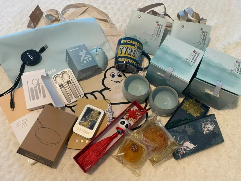 Assorted trade show giveaways including tea sets, wireless chargers, data cables, panda keychains, tote bags, and scented sachets
