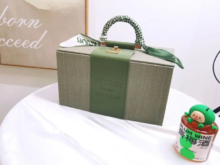 Elegant corporate gift box with light green textile and olive leather craftsmanship, displayed on a desk with a bottle of custom ume liquor, cover image for Inside the Gift Industry article
