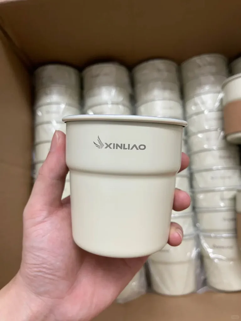A person holding an ivory white stainless steel coffee cup to inspect its details, with a gift box of coffee cups in the background — perfect for trade show giveaways and one of the best trade show giveaways.