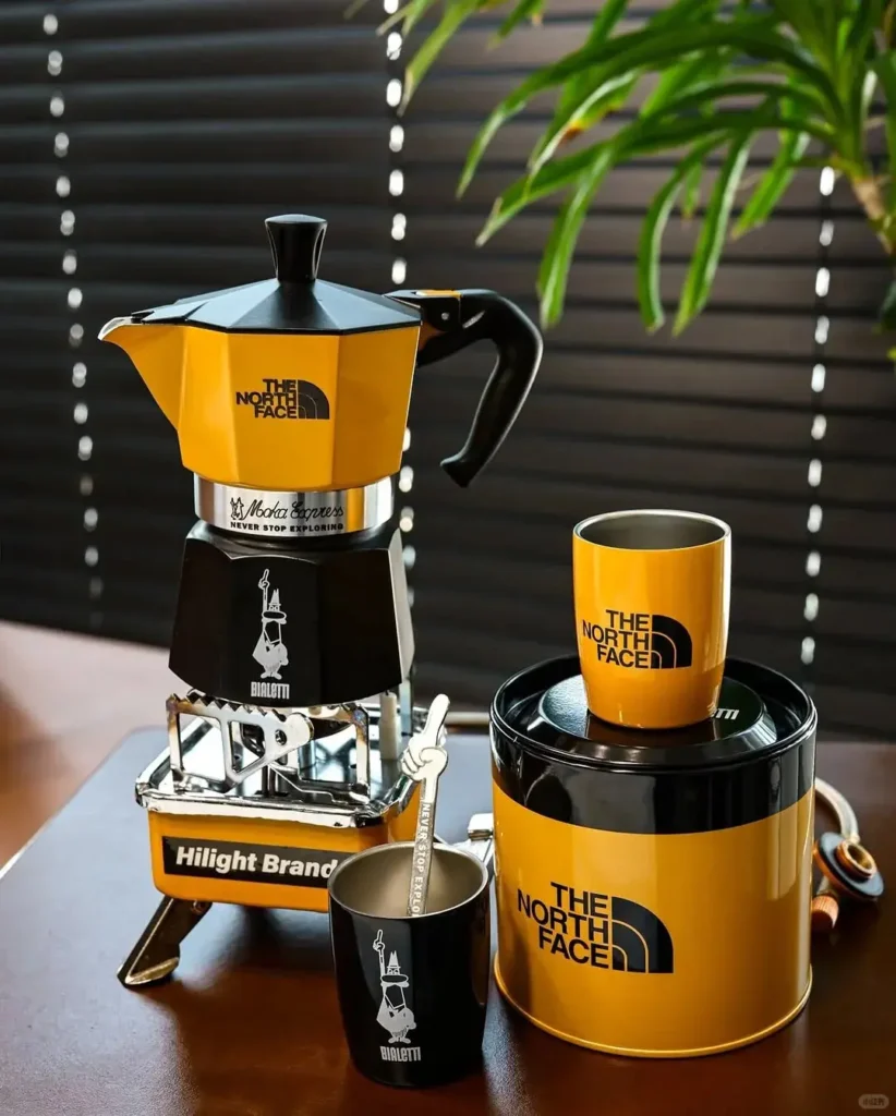 The North Face employee coffee gift set displayed on a desk, featuring a 3-cup coffee maker, two metallic cups with matching spoons, and a Perfetto Moka Classico coffee blend.