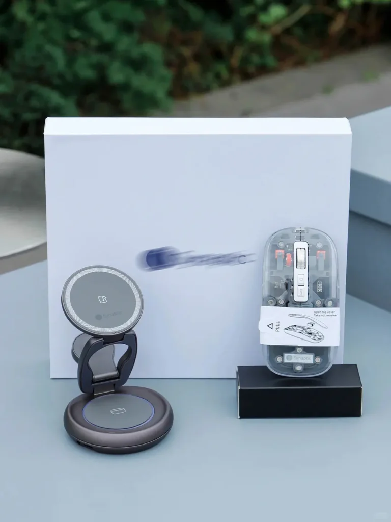 Τεχνολογικά αντικείμενα της εταιρείας, όπως ένα διαφανές ποντίκι Bluetooth και ένας πτυσσόμενος ασύρματος φορτιστής, που εμφανίζονται σε ένα γραφείο από ένα λευκό κουτί δώρου.