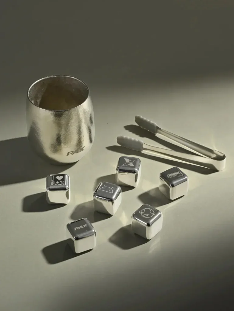 Close-up of a titanium cup, six branded ice cubes, and an ice tong on a table, showcasing premium branded merchandise.
